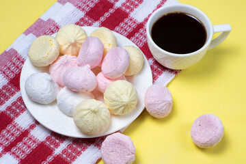 Obraz na płótnie Canvas Small homemade meringue kisses. Meringue cookies and coffee cup on red tablecloth and yellow background.