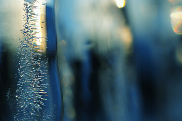 Fototapeta na wymiar Background of icicles in the rays of a winter sunset close up. Dark blue ice backdrop. Frozen water with air bubbles. Tinted blue-green wallpaper on the theme of the cold harsh season. Macro