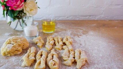 Making homemade cakes. Raw dough, butter, sugar, roses for making brushwood on a wooden tabletop. Concept on a white brick wall background. Homemade food during quarantine and lockdown.