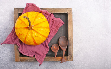 Yellow pumpkin, napkin, wooden spoons in a square box on a gray background.
