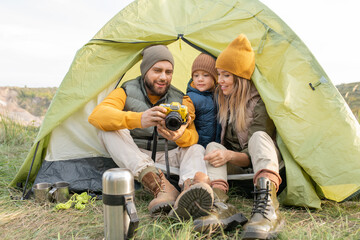 Young bearded man showing photos in photocamera to his son and wife