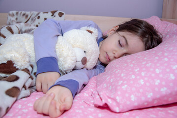 Fototapeta na wymiar Sweet little girl sleeps with a toy teddy bear. Young girl hug teddy bear. It's bedtime for little girl and bear.