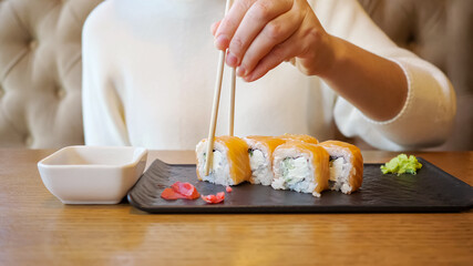 Young unrecognizable woman eating rolls with salmon while sitting in a cafe.