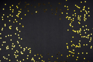 Golden star shape confetti frame on black background. Christmas, New Year, magic concept. Top view, flat lay, copy space.