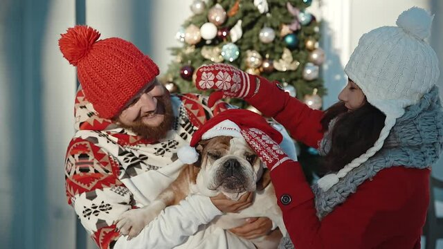 Couple And Their Dog in santa cap spend time together kissing and hugging at xmas eve. Winter holidays concept. Young people love each other. Pet lovers with their doggy
