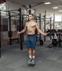 Fototapeta premium Muscular sport man with a naked torso jumps on a skipping rope in a modern cross gym. Cartio workout, healthy lifestyle