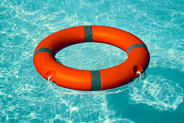 Red lifebuoy pool ring float on blue water. Life ring floating on top of sunny blue water. Life ring in swimming pool
