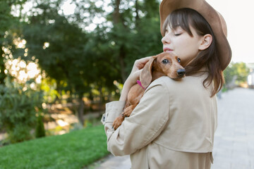 Portrait of a young fashion woman and a lovely dachshund puppy in a city park. Mistress and pet