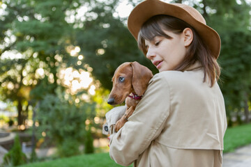 Portrait of a young fashion woman and a lovely dachshund puppy in a city park. Mistress and pet