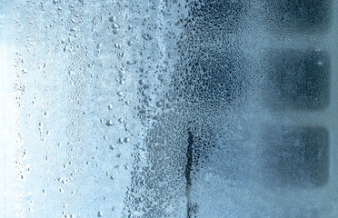 Natural frozen drops of condensation on transparent glass. Beautiful background from a frozen window in winter. Drops texture on the glass