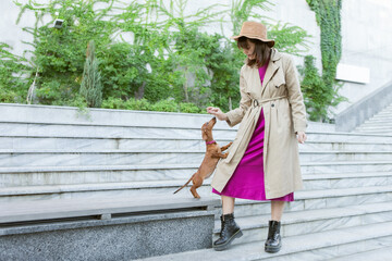 Young fashion woman raising her dachshund puppy outdoors