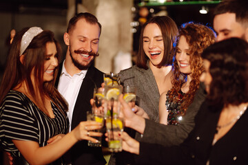 Group of friends cheering and drinking cocktails together at the bar. Young people celebrating winter holiday together with coctails at a nightclub party. Youth, lifestyle, drink, birthday concept.
