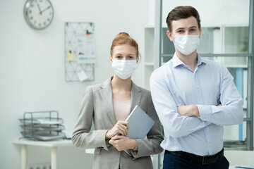 Contemporary office managers in protective masks standing close to each other