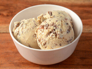 Mocha almond ice cream scoops served in a bowl over a rustic wooden table, selective focus