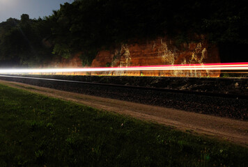 Long time exposure of a car passing on the highway, background of steep rock cliff. Light streaks from the time exposure during late night darkness.