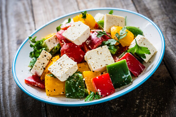 Fresh Greek salad - feta cheese, tomatoes, cucumber, three color pepper, black olives and onion on wooden table
