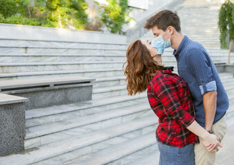 Young Couple in love, man and woman kissing each other in protective medical mask on face outdiir. Environmental pollution concept. Pandemic coronavirus( covid-19), virus protection