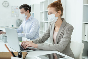 Obraz premium Female in protective mask and her male co-worker working with online data
