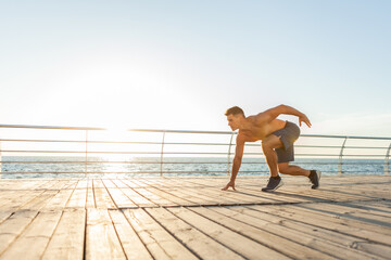 Muscular man with naked torso ready to run at sunrise on the beach