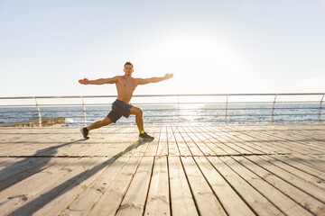 Young muscular man practicing yoga asana at sunrise on the beach