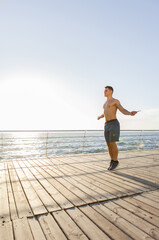 Muscular man athlete jumping rope on the beach at sunrise. Healthy lifestyle concept