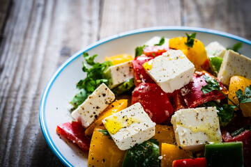 Fresh Greek salad - feta cheese, tomatoes, cucumber, three color pepper, black olives and onion on wooden table
