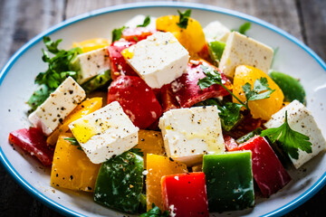 Fresh Greek salad - feta cheese, tomatoes, cucumber, three color pepper, black olives and onion on wooden table

