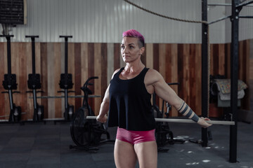 Fototapeta na wymiar Extraordinary muscular powerful woman with pink hair is practicing warm-up before intense workout in a modern cross-gym.