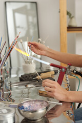 Hands of professional lampworker sitting by table and burning glass workpiece