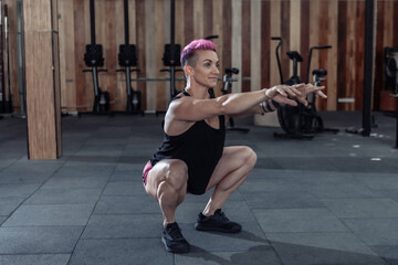 Fototapeta na wymiar Extraordinary muscular powerful woman with pink hair is practicing warm-up before intense workout in a modern cross-gym.