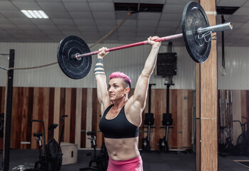 Powerful and strong woman bodybuilder doing overhead with heavy barbell in modern cross gym. Functional training. Bodybuilding and Fitness