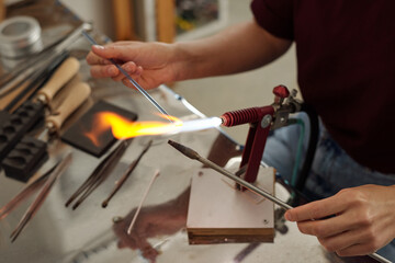 Hands of young female lampworker holding two workpieces over burner