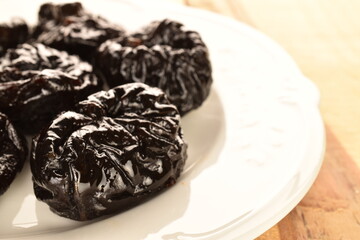 Sweet organic prunes with a ceramic plate, close-up, on a wooden table.