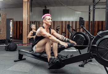 Fototapeta na wymiar Muscular sporty women workout on training simulator in crossfit gym. Sportswomen exercising on rowing machines