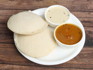 Idli or idly is a healthy Indian, vegetarian, traditional and popular steam cooked rice cakes served with bowls of chutney and sambar as side dishes.selective focus
