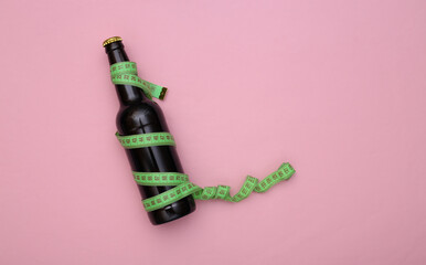Diet concept. A bottle of beer wrapped in a measuring tape on a pink pastel background. Top view