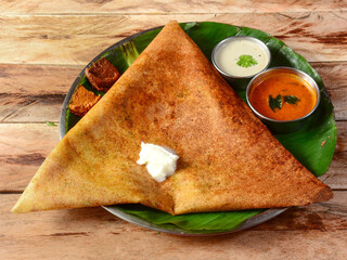 Mysore Masala dosa, a famous south Indian traditional breakfast with filling of a mixture of mashed potatoes served with different chutney and sambar over a rustic wooden background, selective focus