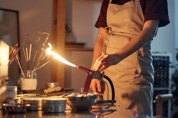 Hands of female lampworker in apron standing by workplace and regulating burner