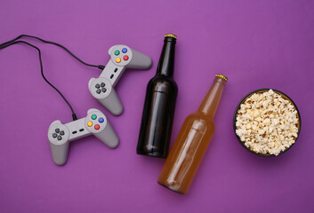 Naklejka premium Entertainment time. Gamepads and popcorn bowl, beer bottles on purple background. Top view