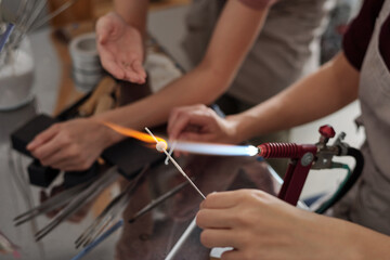 Hands of young female artisan burning glass workpiece while holding it on fire