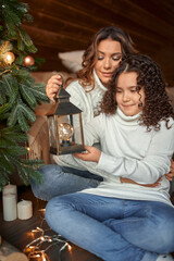 The pretty girl with mum are decorating a Christmas tree in the house. Happy family.