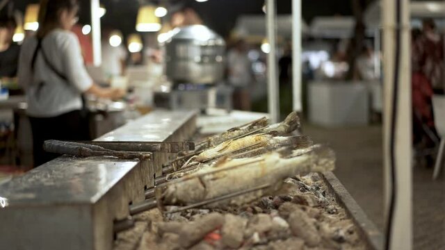 Handheld shot of frying fish on a skewers, street food market in Singapore. Rows of small fishes being fried spinning on skewers at street food local market