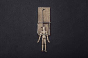 Wooden puppet caught by a mousetrap on a black background