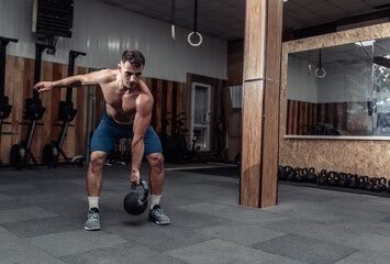 Fototapeta na wymiar Muscular powerful man exercising with heavy kettlebell in cross fit gym. Functional training with free weights