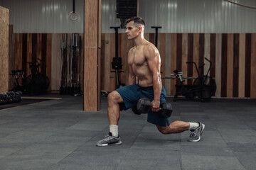 Fototapeta na wymiar Muscular man training his legs, doing lunges with heavy dumbbells in modern gym. Healthy lifestyle concept