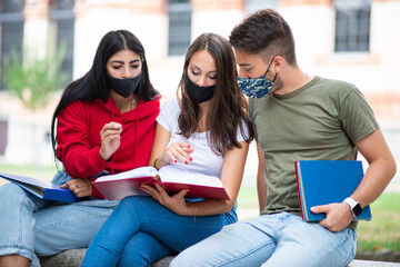 Students studying together sitting on a bench outdoor and wearing masks during coronavirus times