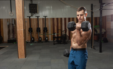 Fototapeta na wymiar Muscular man is exercising with heavy dumbbells, training biceps in the gym. Healthy lifestyle