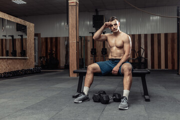 Fototapeta na wymiar Tired athletic man is resting after an intense workout while sitting on a bench in the gym.