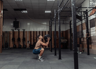 Fototapeta na wymiar Athletic male bodybuilder exercises with medicine ball in the gym. Functional training