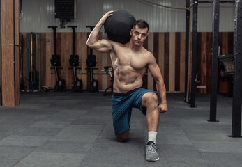 Obraz na płótnie Canvas Athletic male bodybuilder exercises with heavy medicine ball in the gym. Functional training